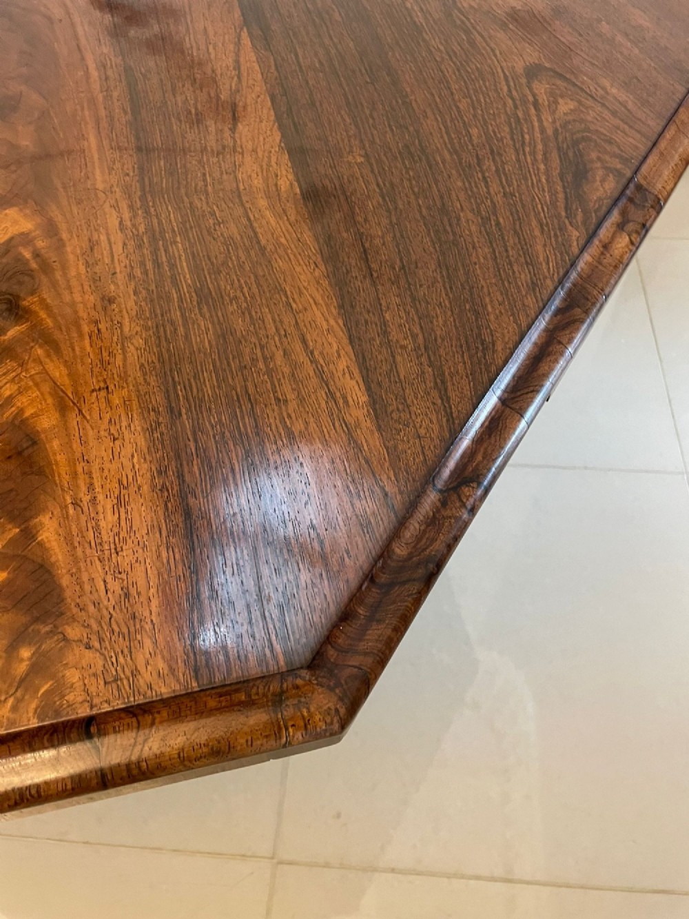 An Early Victorian octagonal rosewood tilt-top centre table with a highly figured grain surface resting on a carved pedestal base with scroll feet. View V