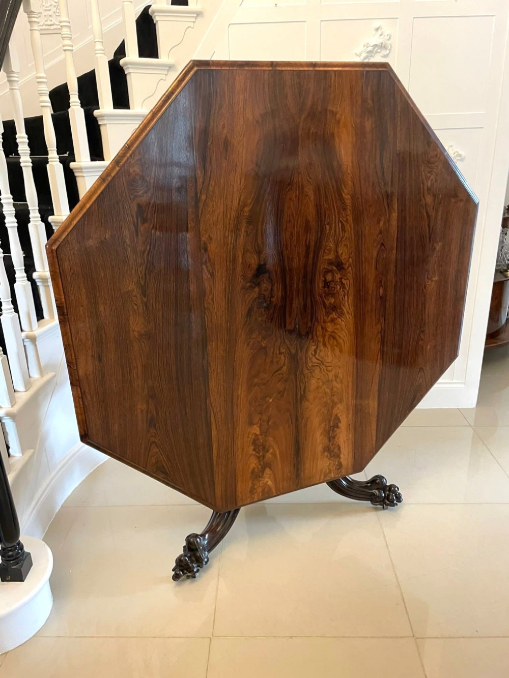 An Early Victorian octagonal rosewood tilt-top centre table with a highly figured grain surface resting on a carved pedestal base with scroll feet.