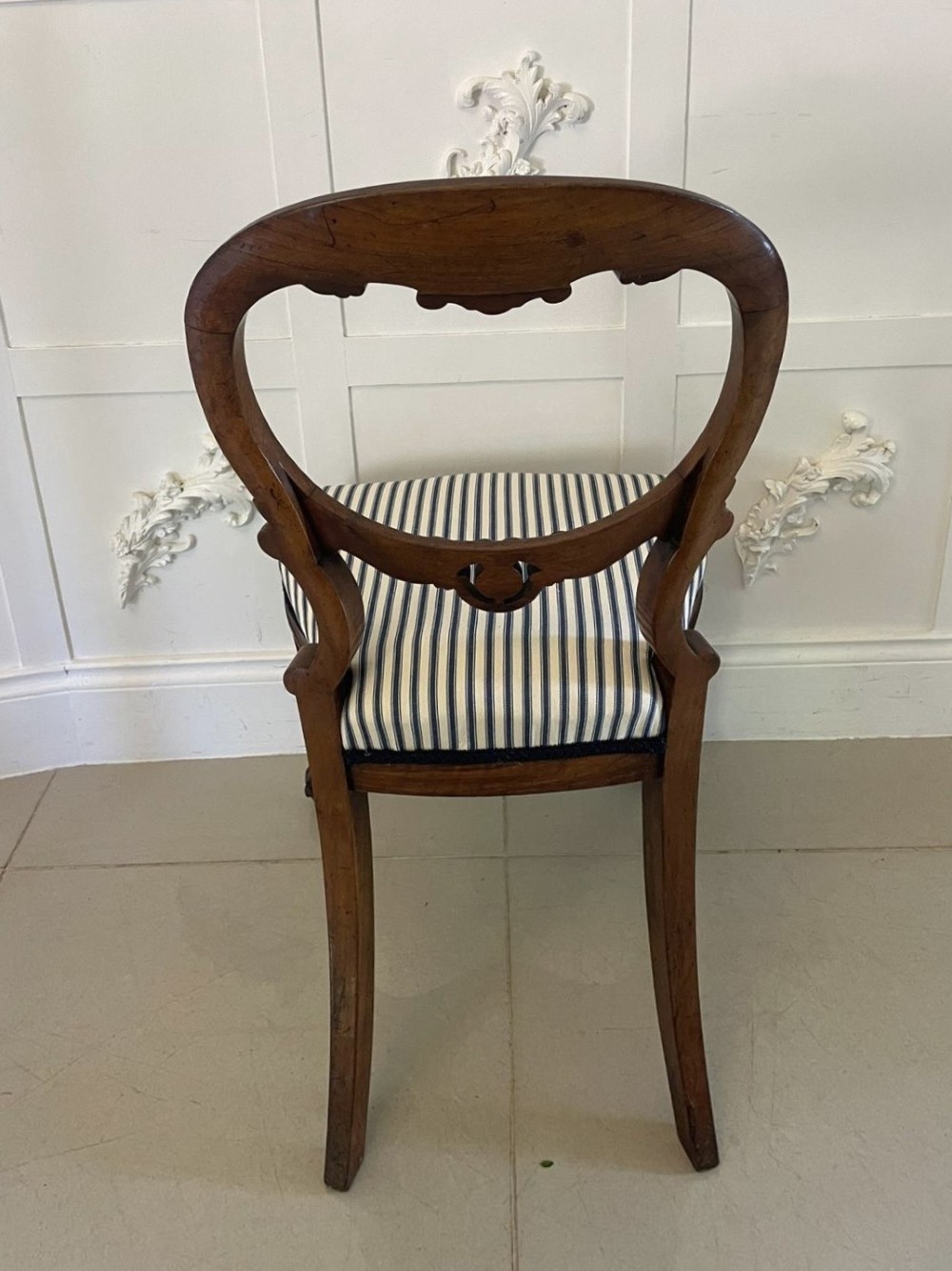 A set of six Victorian carved walnut dining chairs featuring rounded balloon backs, carved foliage detailing, cabriole front legs, and blue and white striped upholstered seats. View II