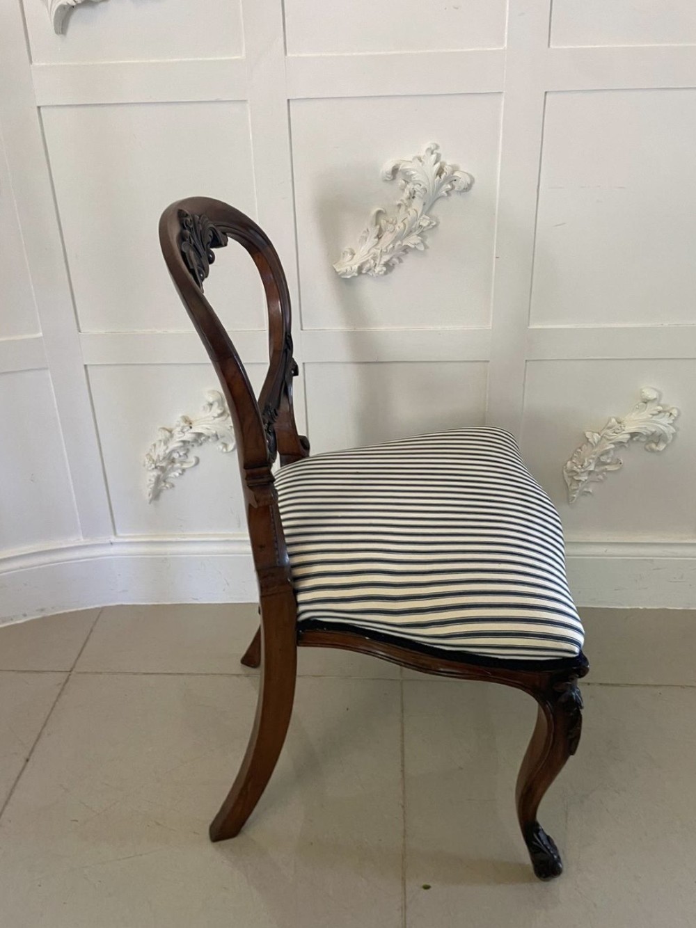 A set of six Victorian carved walnut dining chairs featuring rounded balloon backs, carved foliage detailing, cabriole front legs, and blue and white striped upholstered seats. View V