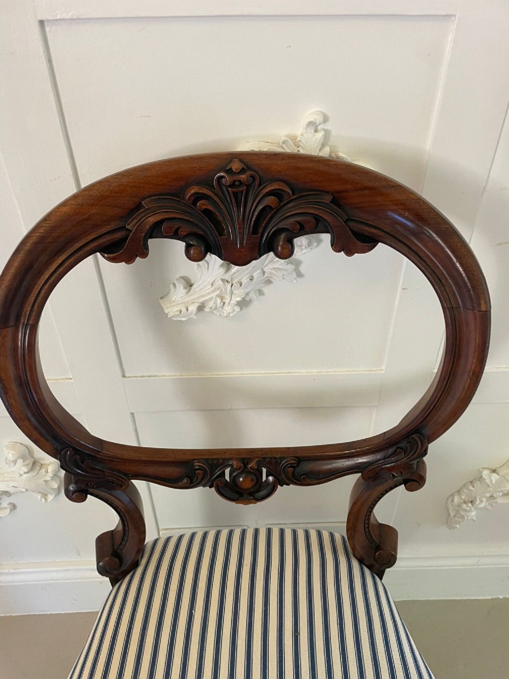 A set of six Victorian carved walnut dining chairs featuring rounded balloon backs, carved foliage detailing, cabriole front legs, and blue and white striped upholstered seats. View VII