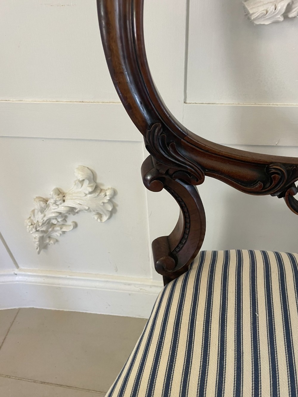 A set of six Victorian carved walnut dining chairs featuring rounded balloon backs, carved foliage detailing, cabriole front legs, and blue and white striped upholstered seats. View VIII
