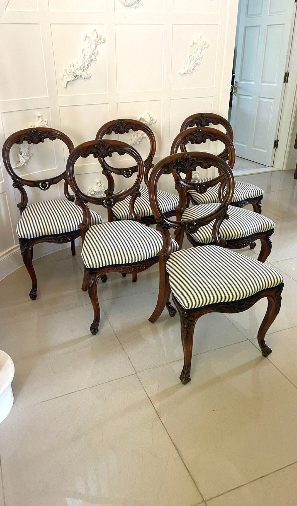 A set of six Victorian carved walnut dining chairs featuring rounded balloon backs, carved foliage detailing, cabriole front legs, and blue and white striped upholstered seats. View X