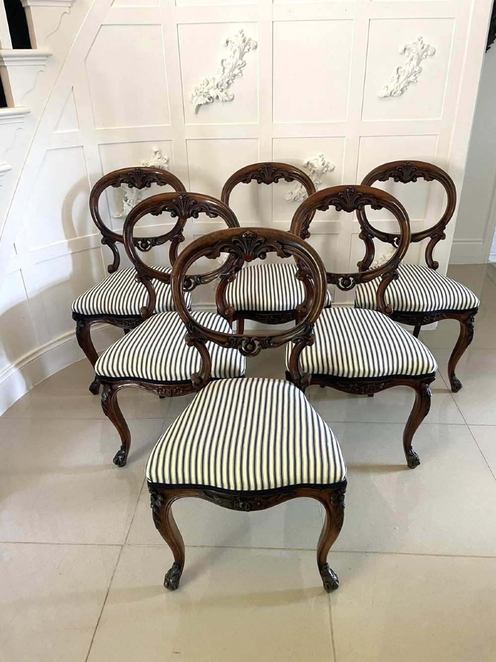 A set of six Victorian carved walnut dining chairs featuring rounded balloon backs, carved foliage detailing, cabriole front legs, and blue and white striped upholstered seats. View XI
