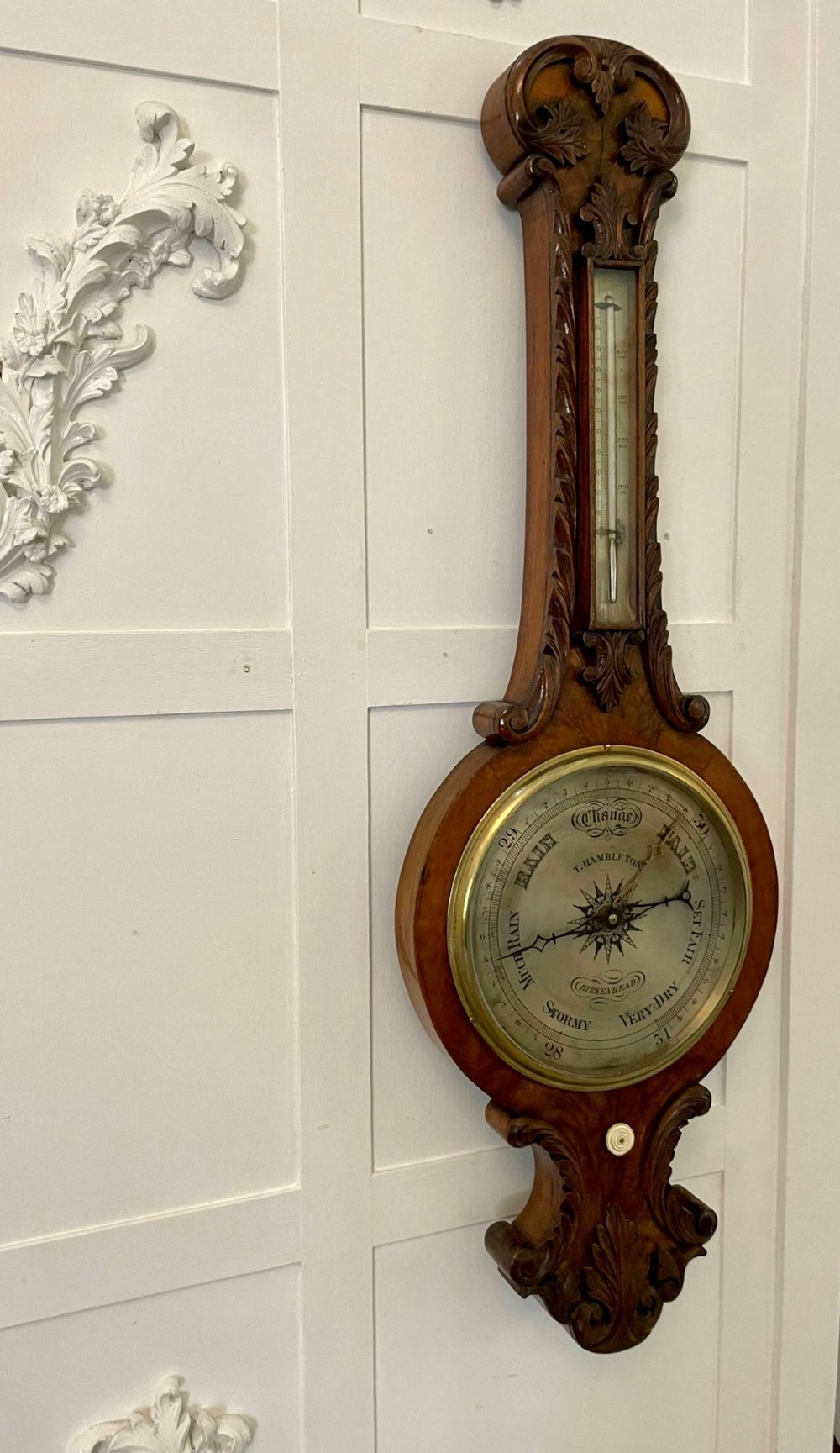 Victorian wall-mounted banjo barometer crafted from carved burr walnut featuring an upper glass thermometer gauge and a lower silvered dial in a brass frame. View V
