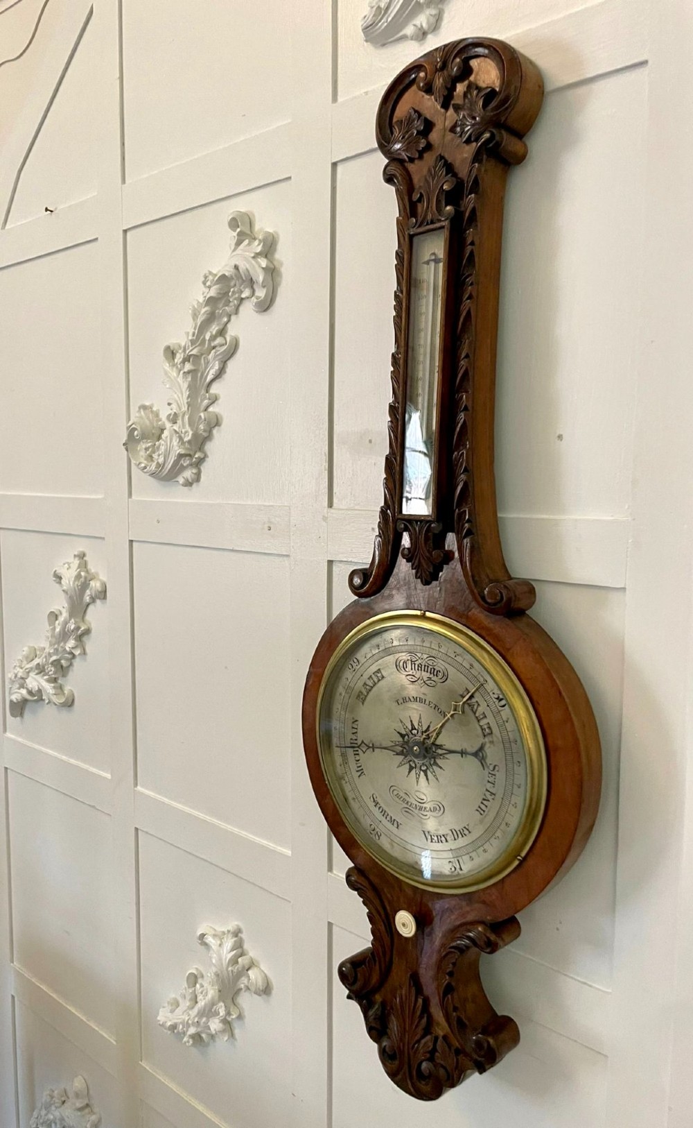 Victorian wall-mounted banjo barometer crafted from carved burr walnut featuring an upper glass thermometer gauge and a lower silvered dial in a brass frame. View VI