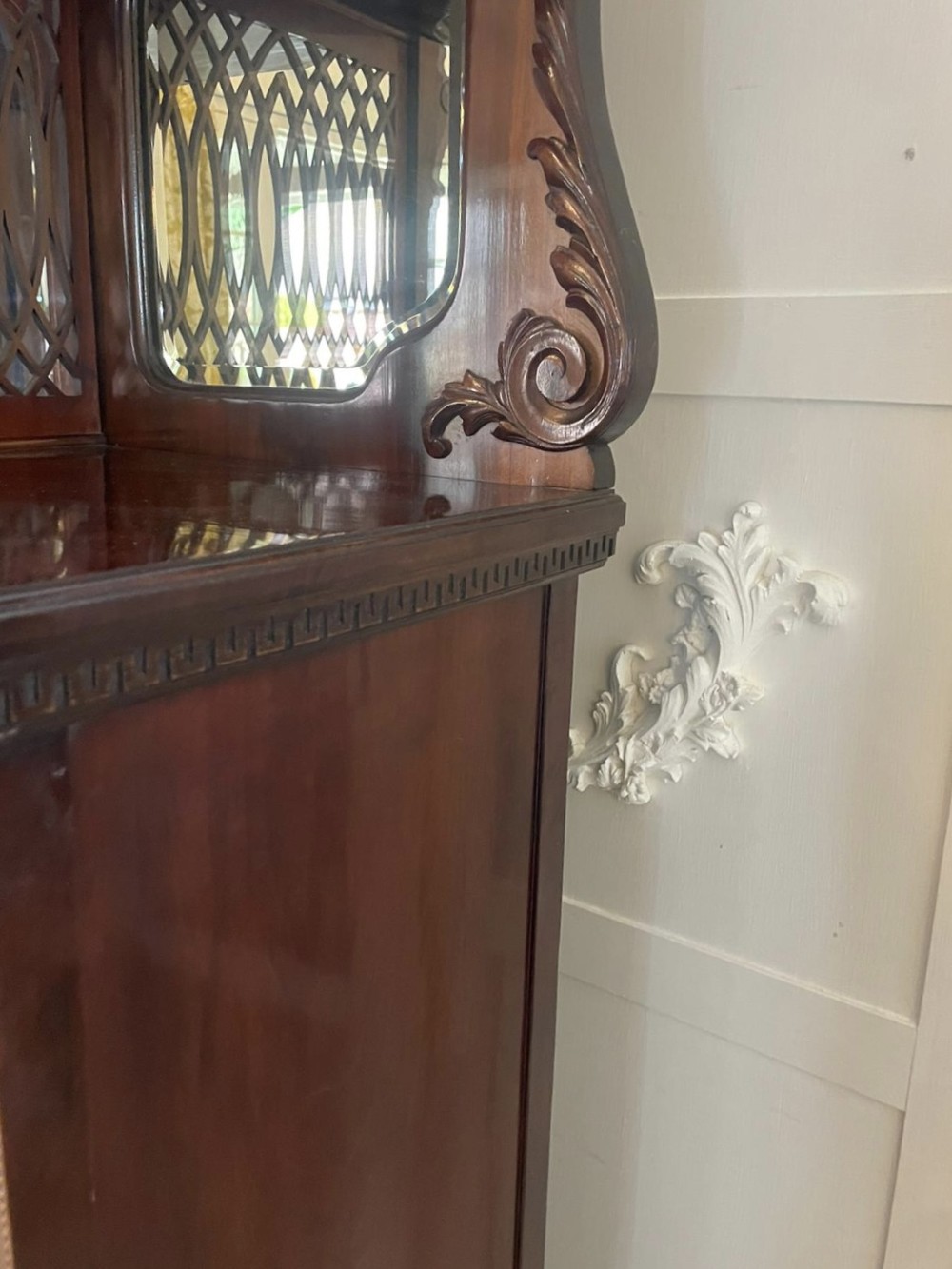 A large Victorian mahogany display cabinet featuring a carved pediment top, central bevelled mirror back, floral satinwood marquetry panel, glazed doors, and a bottom shelf. View VII