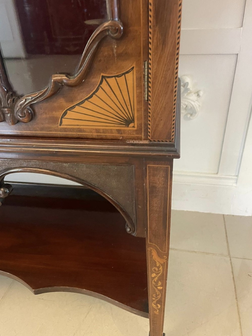 A large Victorian mahogany display cabinet featuring a carved pediment top, central bevelled mirror back, floral satinwood marquetry panel, glazed doors, and a bottom shelf. View VIII