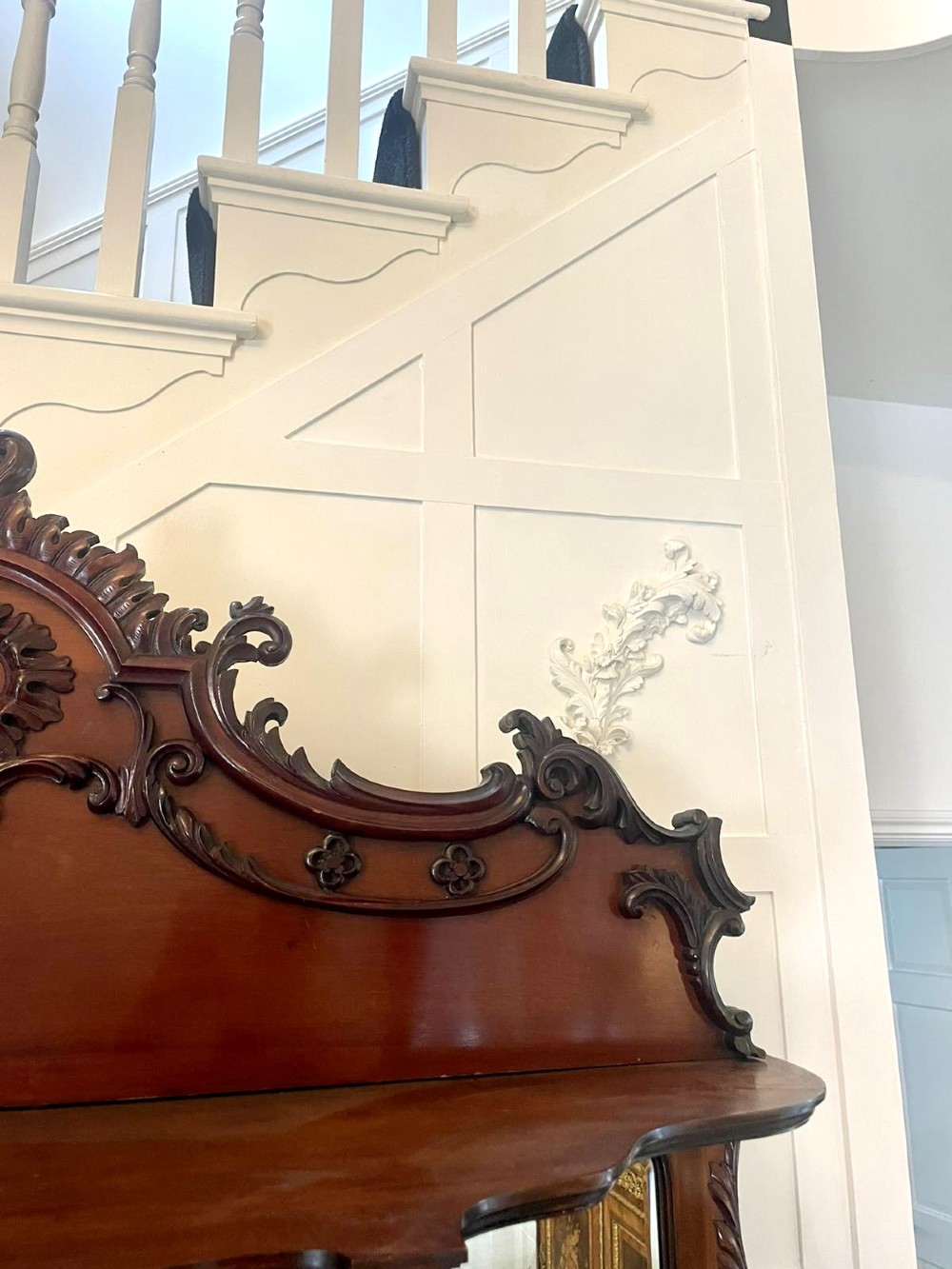 A large Victorian mahogany display cabinet featuring a carved pediment top, central bevelled mirror back, floral satinwood marquetry panel, glazed doors, and a bottom shelf. View X