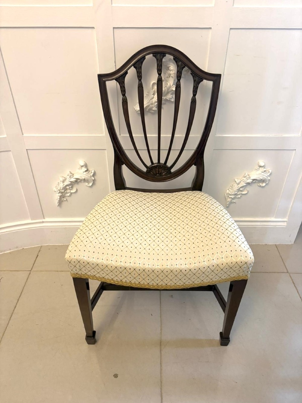 A set of ten antique Edwardian mahogany dining chairs featuring carved shield-shaped backrests and light cream upholstered seats. View XIII