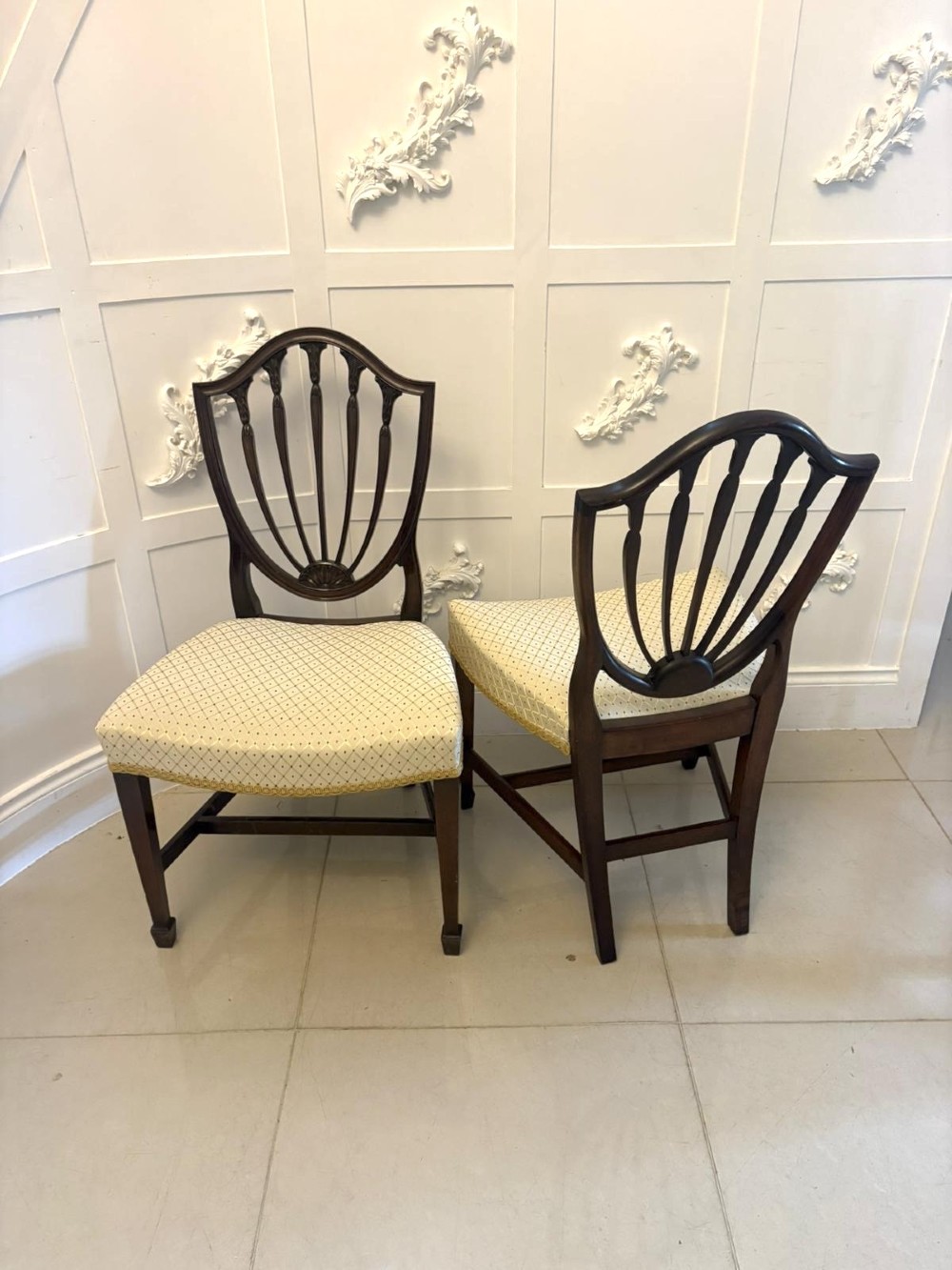 A set of ten antique Edwardian mahogany dining chairs featuring carved shield-shaped backrests and light cream upholstered seats. View XV