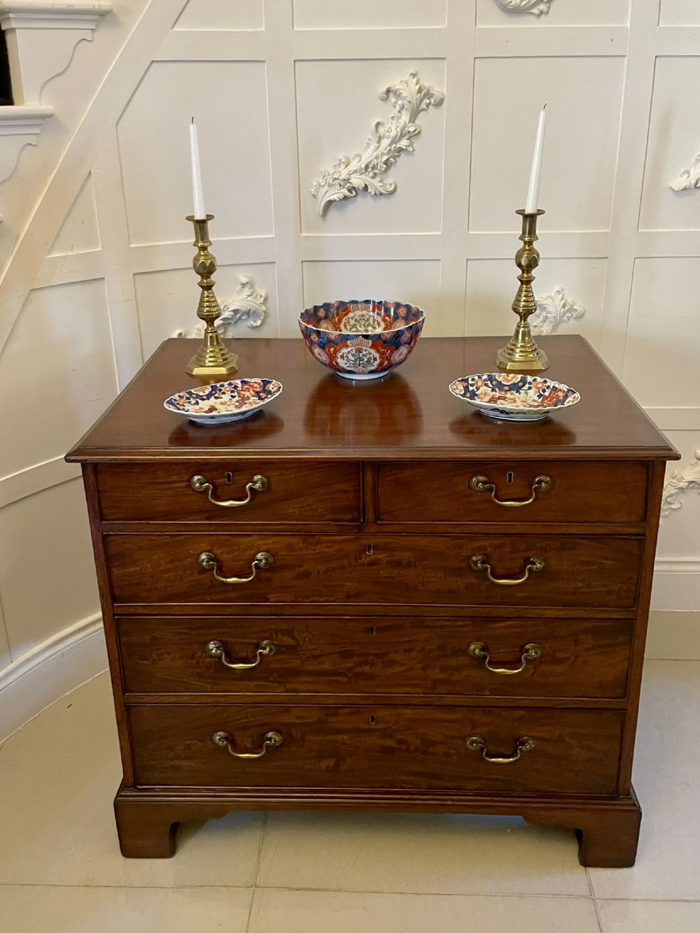 A George III mahogany chest of drawers featuring a two-over-three drawer configuration with brass swan-neck handles on bracket feet. View II