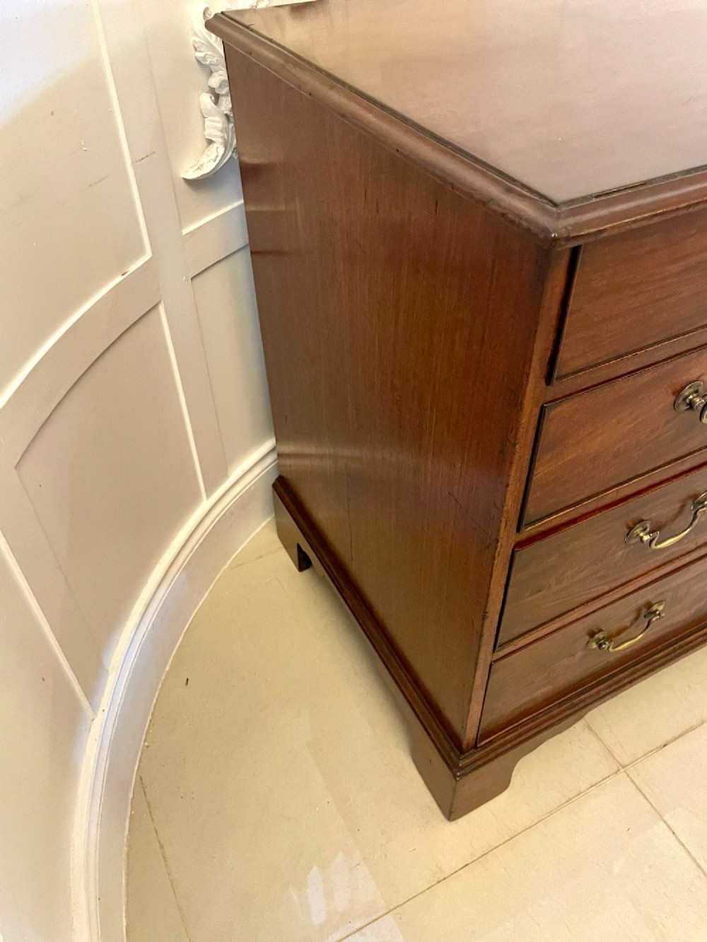 A George III mahogany chest of drawers featuring a two-over-three drawer configuration with brass swan-neck handles on bracket feet. View V
