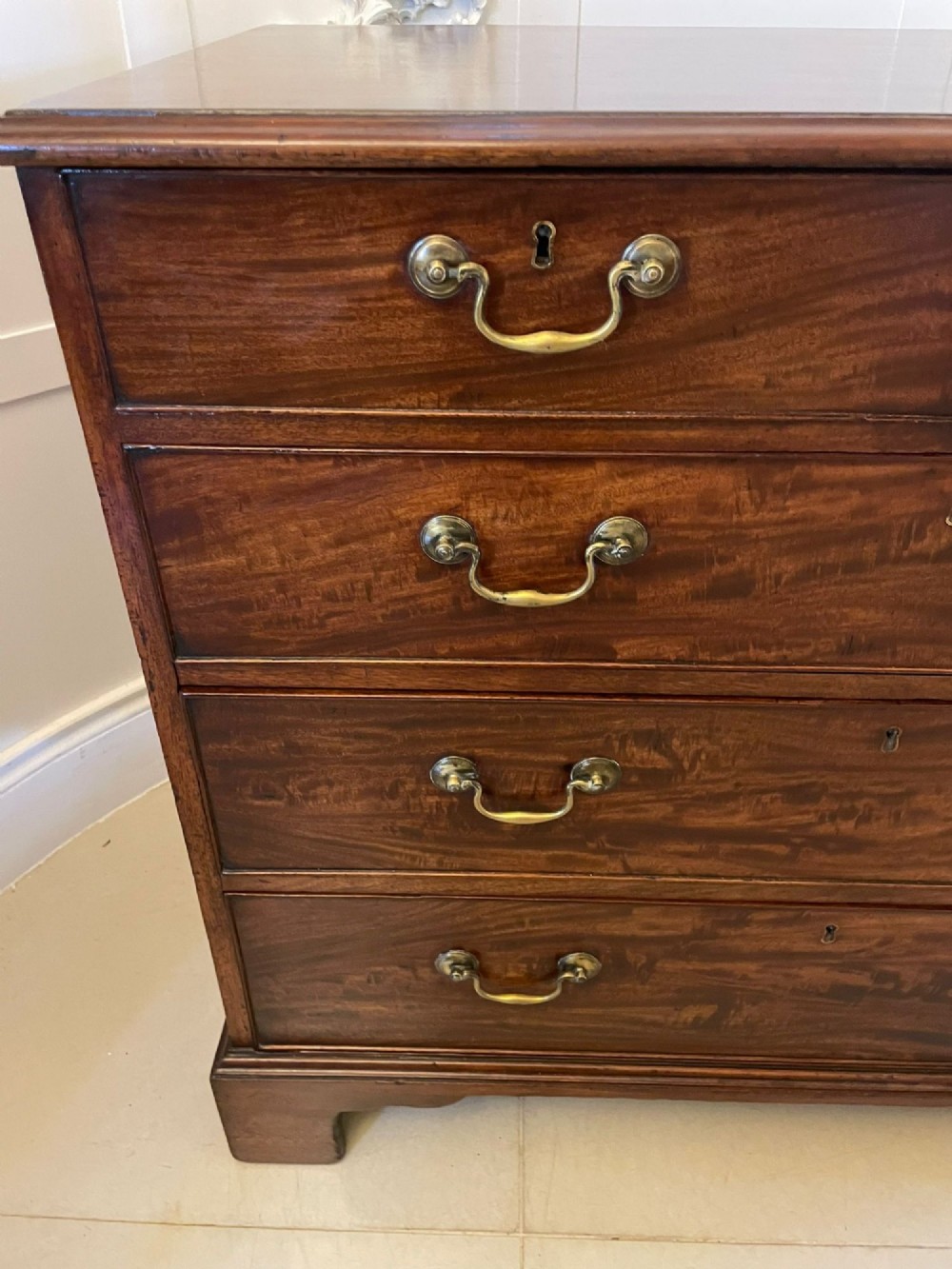 A George III mahogany chest of drawers featuring a two-over-three drawer configuration with brass swan-neck handles on bracket feet. View VIII