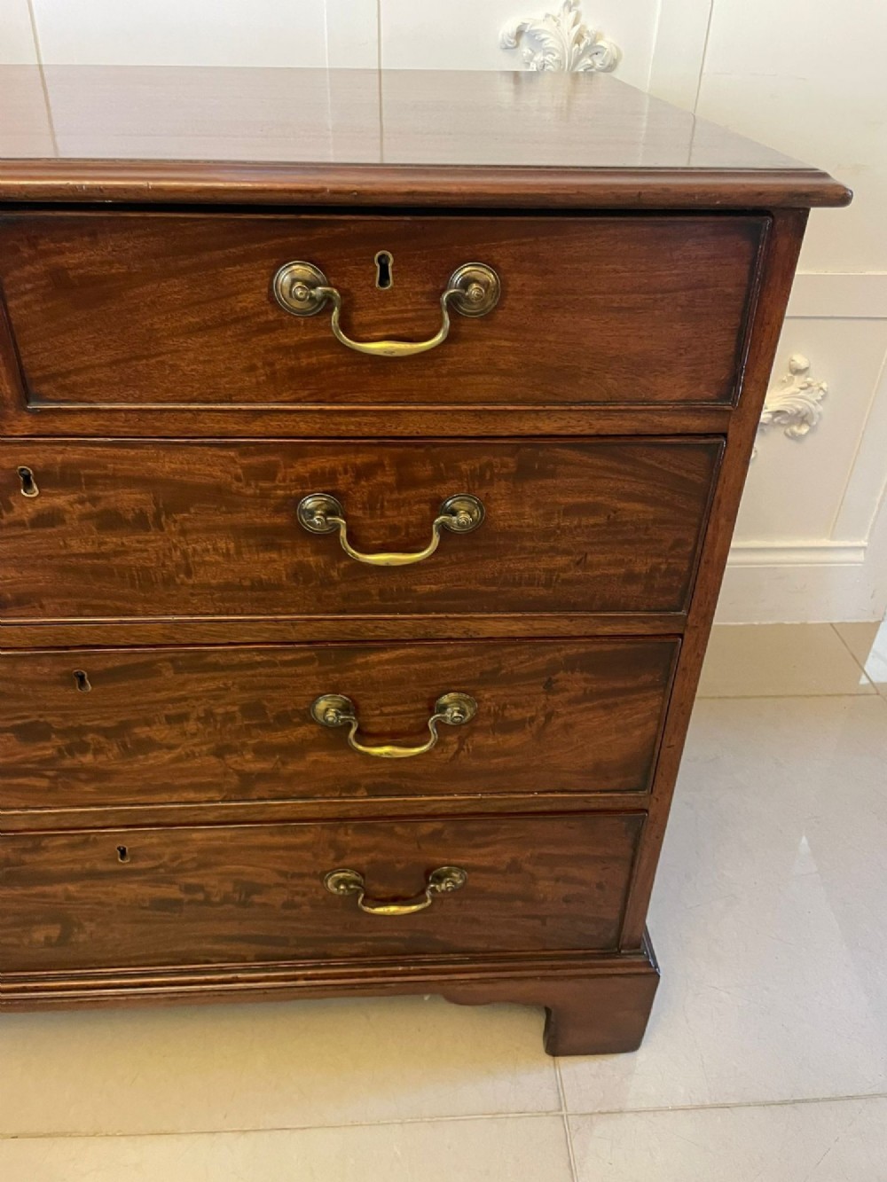 A George III mahogany chest of drawers featuring a two-over-three drawer configuration with brass swan-neck handles on bracket feet. View IX
