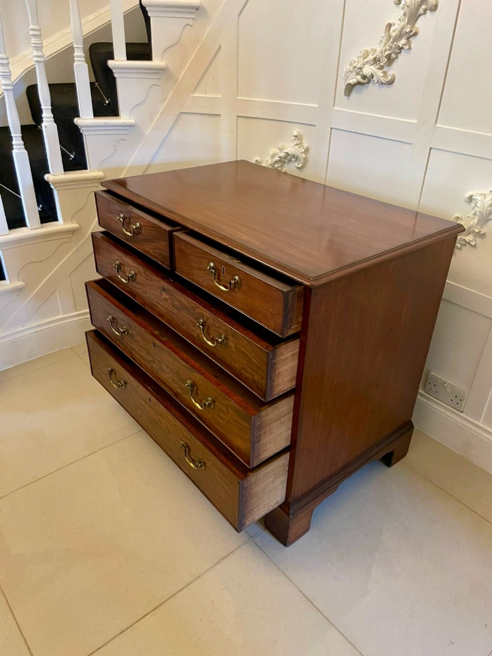 A George III mahogany chest of drawers featuring a two-over-three drawer configuration with brass swan-neck handles on bracket feet. View X