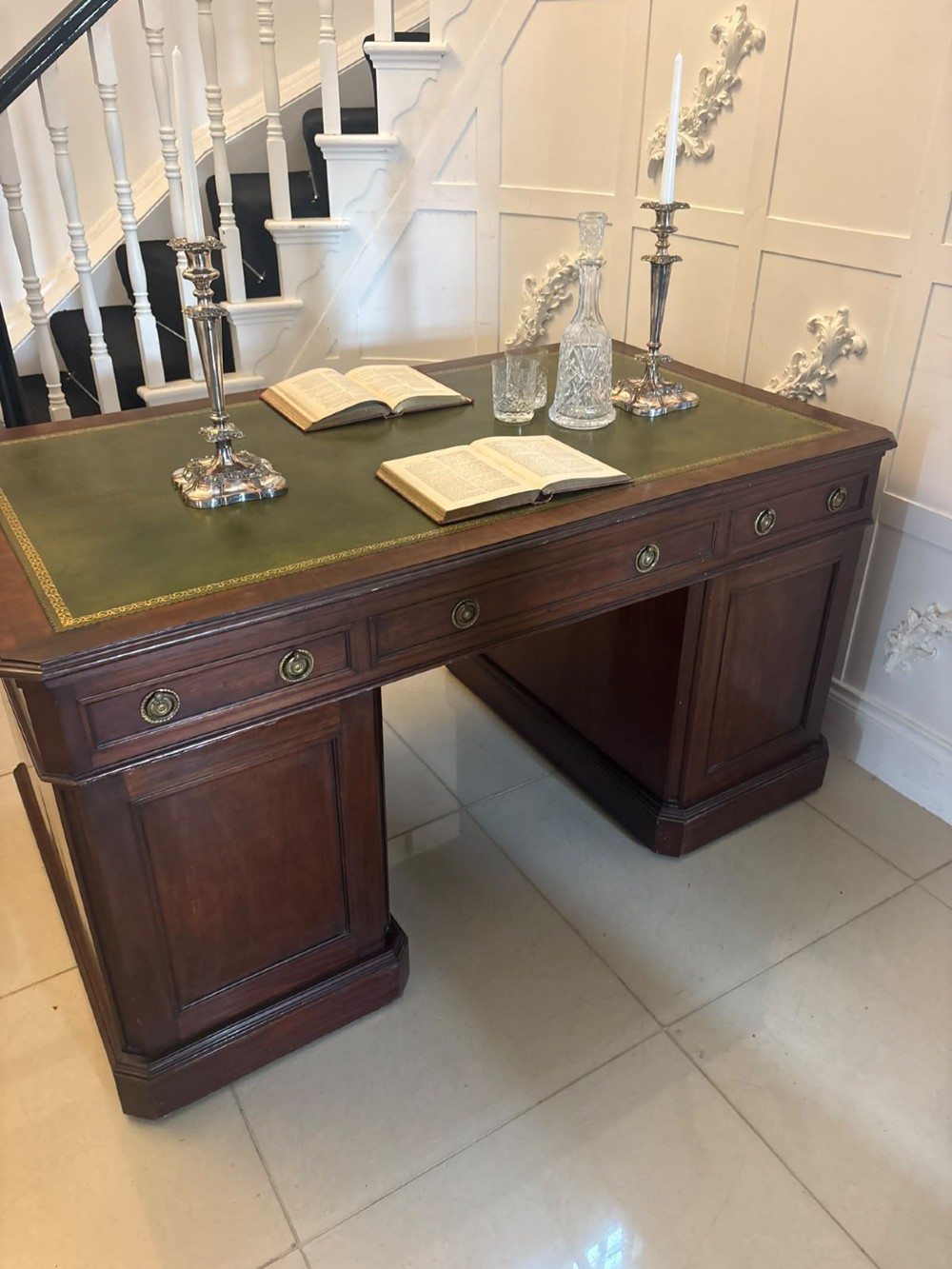 A Victorian mahogany pedestal desk featuring a green leather inset writing surface, brass ring handles, and two drawer pedestals framing a central kneehole. View V