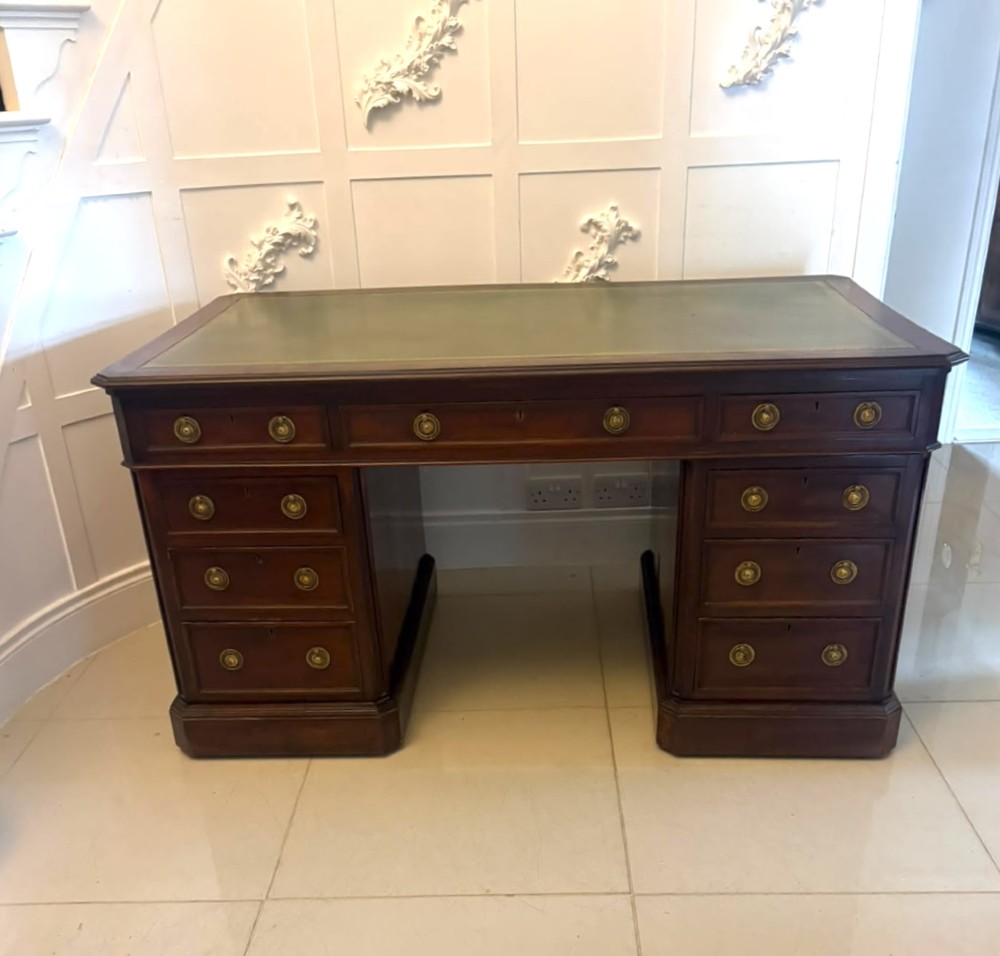 A Victorian mahogany pedestal desk featuring a green leather inset writing surface, brass ring handles, and two drawer pedestals framing a central kneehole. View XV