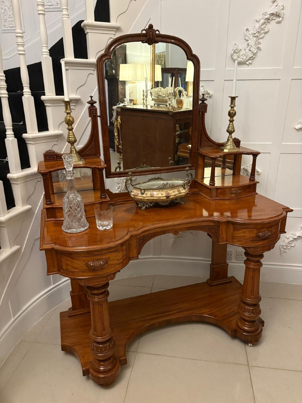 An antique Victorian carved mahogany dressing table featuring an arched swivel mirror, twin trinket drawers, turned front columns, and a shaped lower shelf. View II