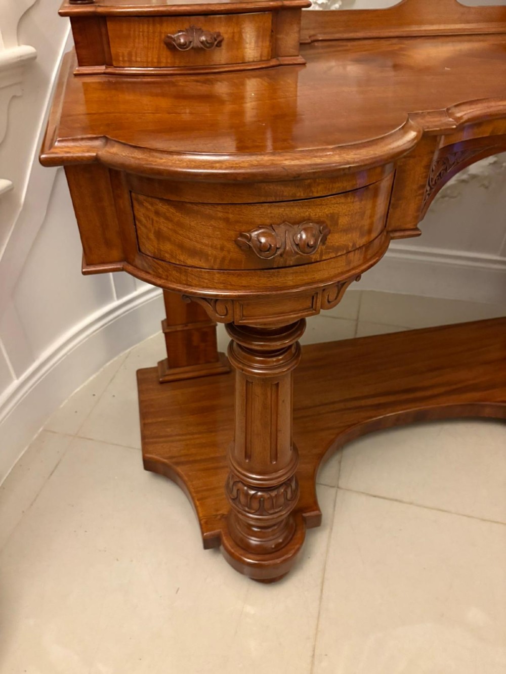 An antique Victorian carved mahogany dressing table featuring an arched swivel mirror, twin trinket drawers, turned front columns, and a shaped lower shelf. View XII