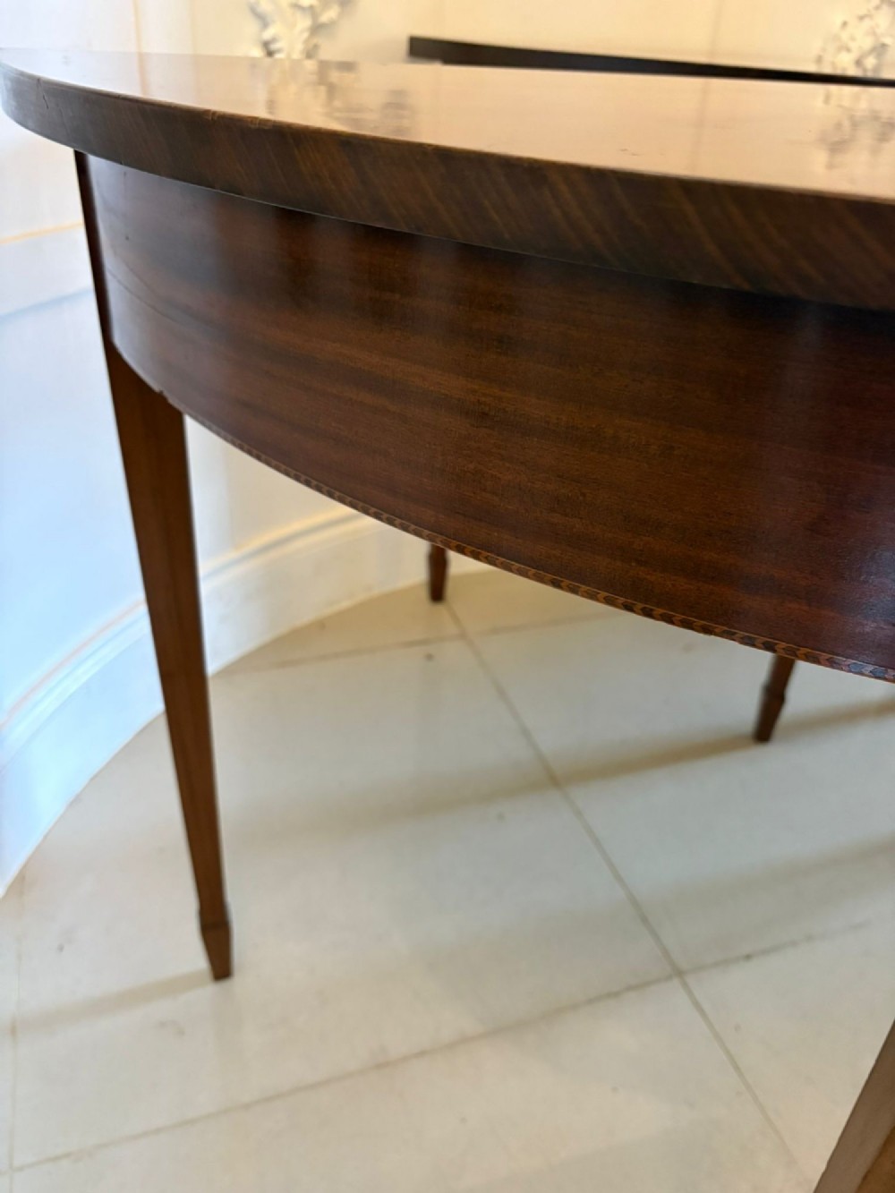 A pair of antique George III semi-circular mahogany console tables with smooth figured tops, apron friezes, and slender tapered legs. View VII