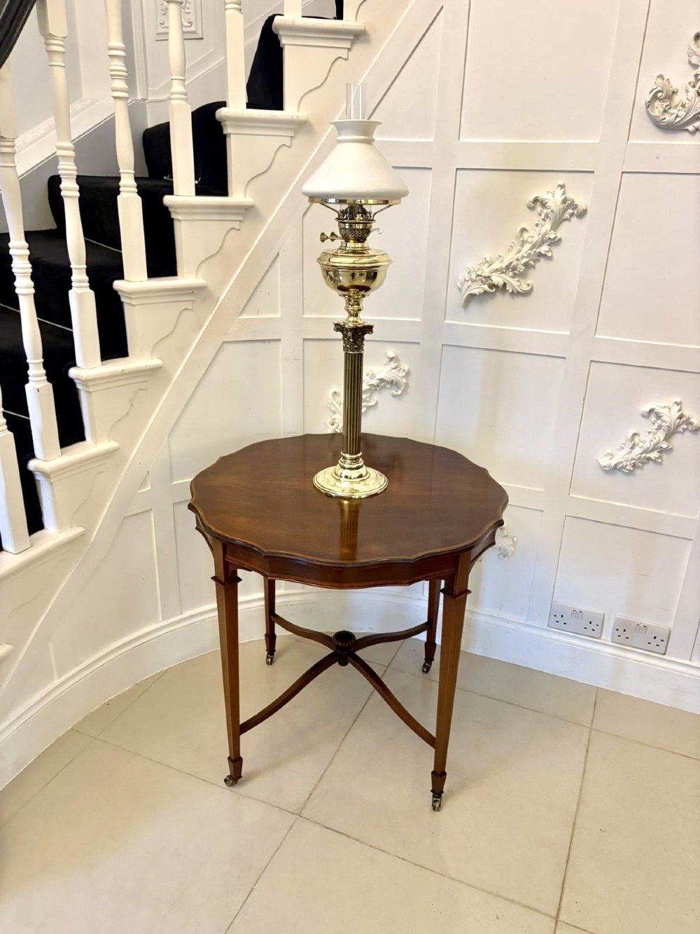 An antique Edwardian polished wood centre table featuring a shaped scalloped top, satinwood inlaid banding, tapered legs with brass castors, and an X-frame stretcher with a central finial. View II