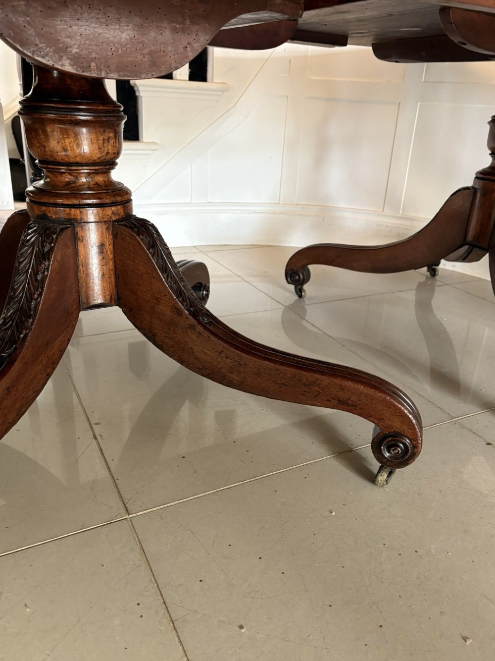 A polished Regency mahogany dining table featuring a three-pillar pedestal base with splayed reeded legs ending in brass castors. View II
