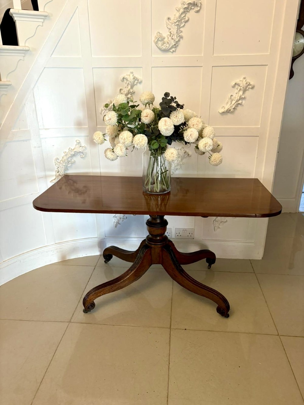 A polished Regency mahogany dining table featuring a three-pillar pedestal base with splayed reeded legs ending in brass castors. View VII