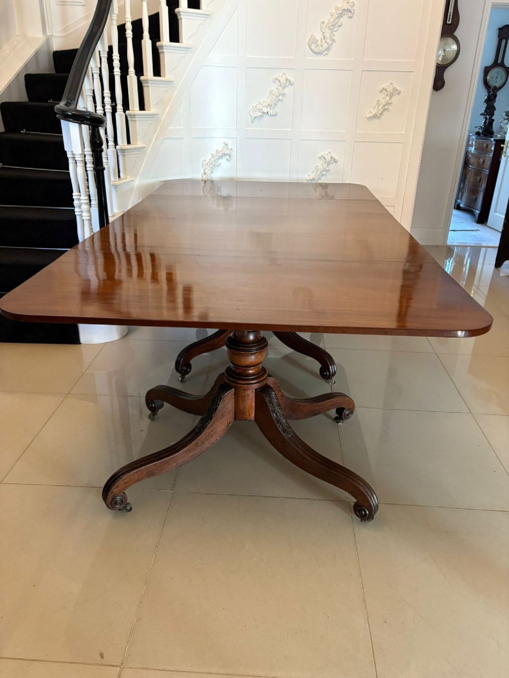 A polished Regency mahogany dining table featuring a three-pillar pedestal base with splayed reeded legs ending in brass castors. View VIII