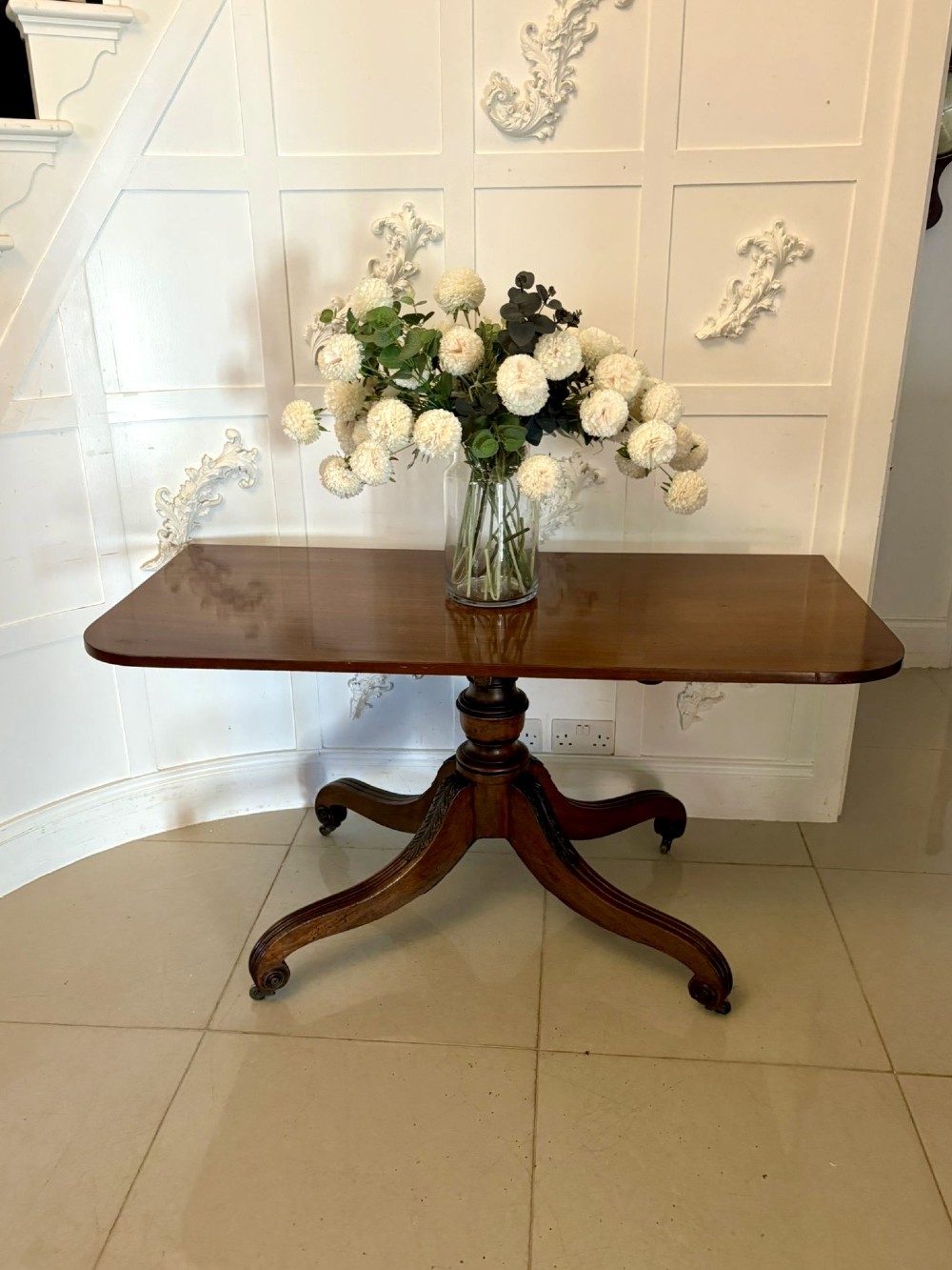 A polished Regency mahogany dining table featuring a three-pillar pedestal base with splayed reeded legs ending in brass castors. View XI