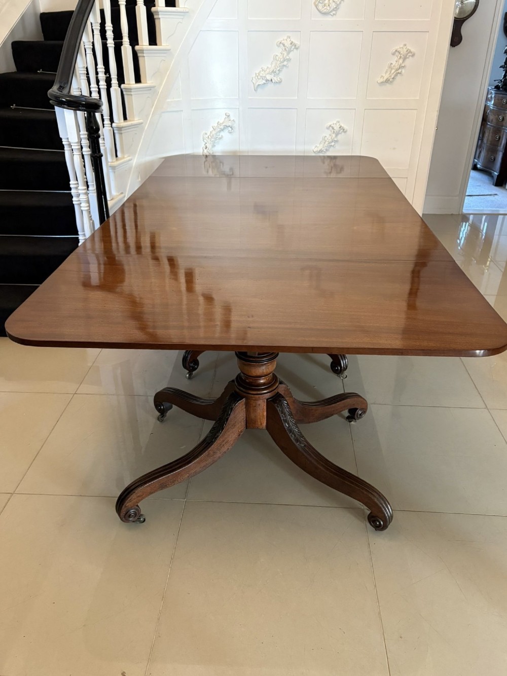 A polished Regency mahogany dining table featuring a three-pillar pedestal base with splayed reeded legs ending in brass castors.