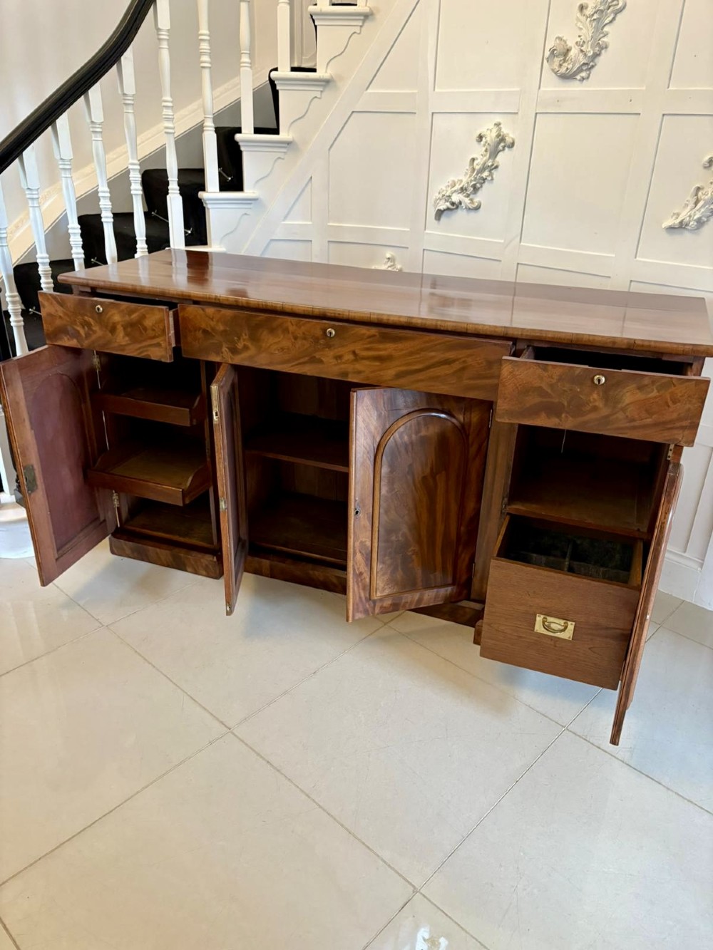 A Victorian figured mahogany sideboard with four arched cupboard doors, three shallow frieze drawers, and a plinth base. View II