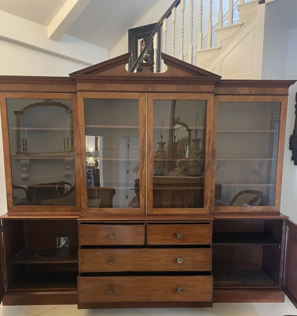 A large George III mahogany breakfront bookcase featuring glazed upper doors topped with a broken swan-neck pediment, set over a base section with drawers and side cupboards. View VII