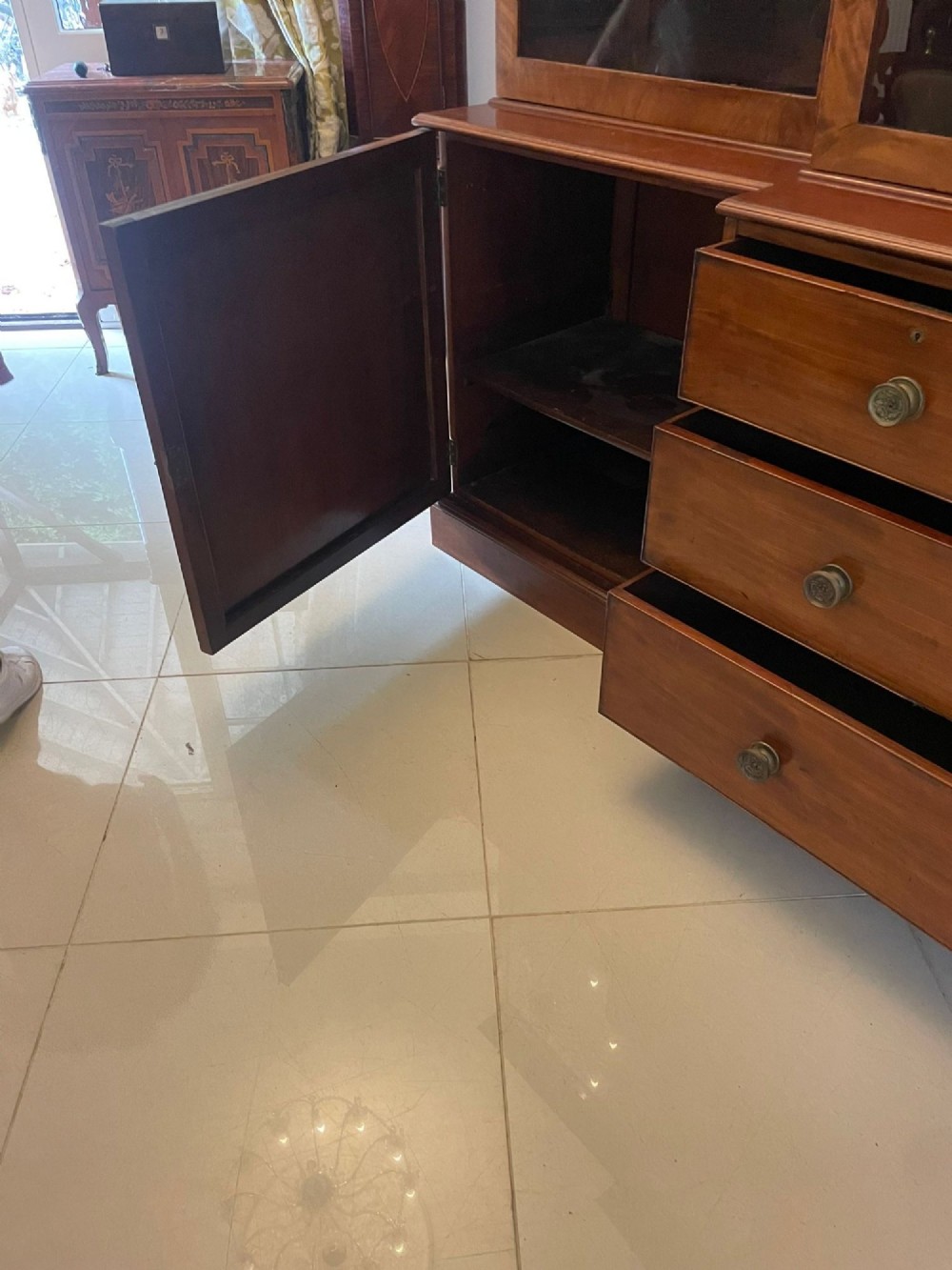 A large George III mahogany breakfront bookcase featuring glazed upper doors topped with a broken swan-neck pediment, set over a base section with drawers and side cupboards. View X
