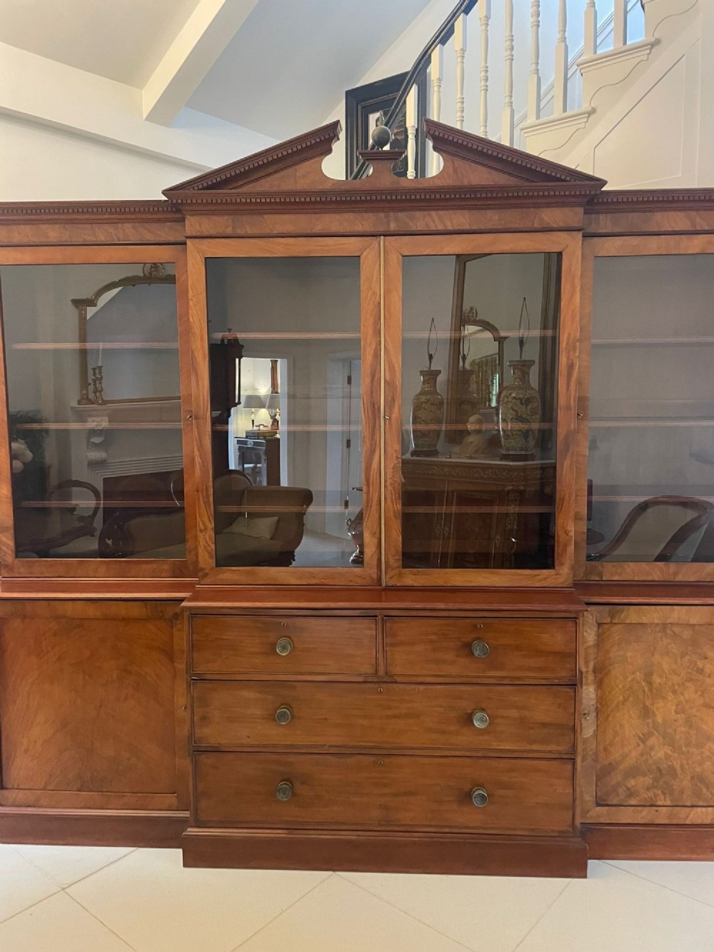A large George III mahogany breakfront bookcase featuring glazed upper doors topped with a broken swan-neck pediment, set over a base section with drawers and side cupboards. View XII