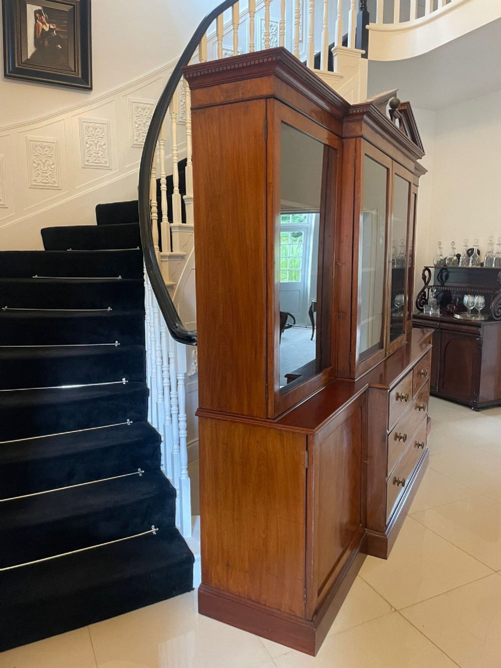 A large George III mahogany breakfront bookcase featuring glazed upper doors topped with a broken swan-neck pediment, set over a base section with drawers and side cupboards. View XIII