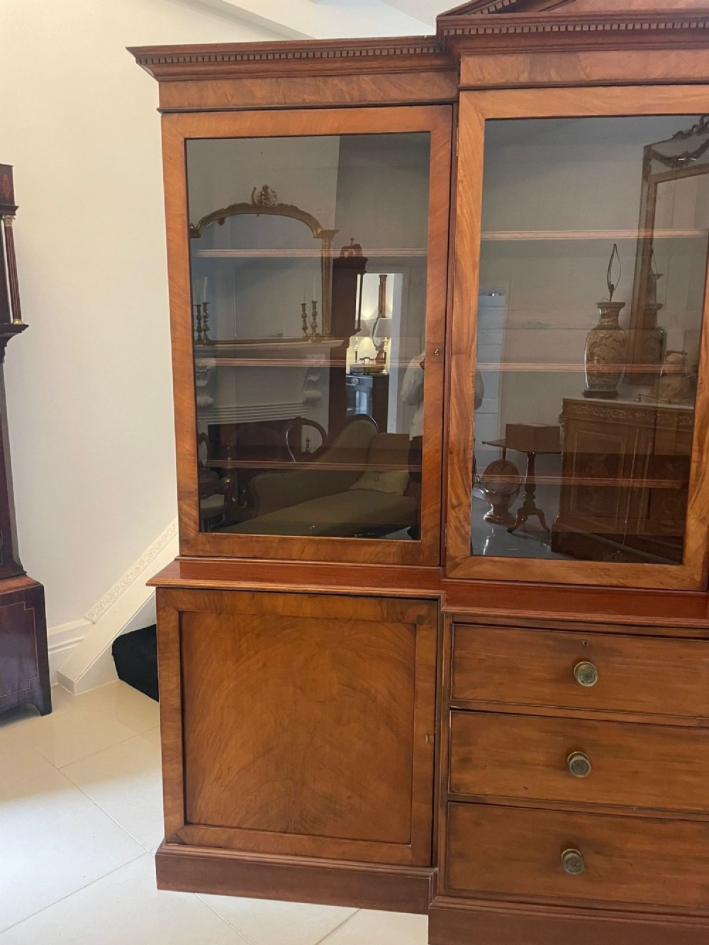 A large George III mahogany breakfront bookcase featuring glazed upper doors topped with a broken swan-neck pediment, set over a base section with drawers and side cupboards. View XV