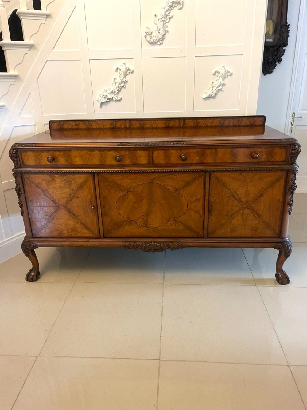 An antique burr walnut sideboard featuring quarter-veneered panel doors, carved edge mouldings, drawers with wooden knobs, and cabriole legs.