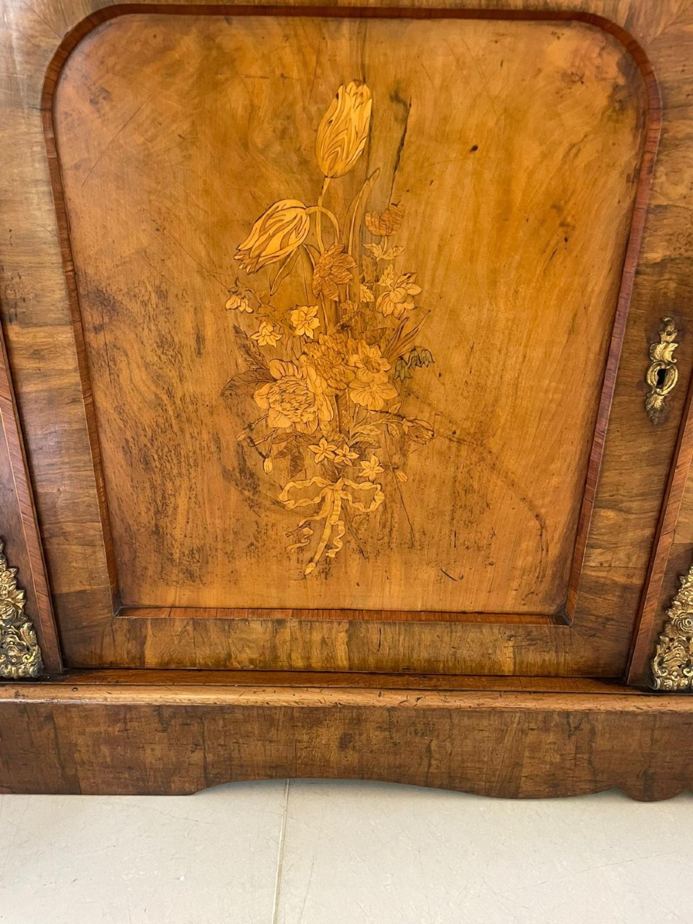 A Victorian two-part burr walnut bookcase cabinet featuring glazed upper doors with floral marquetry inlays and gilt ormolu mounts. View V