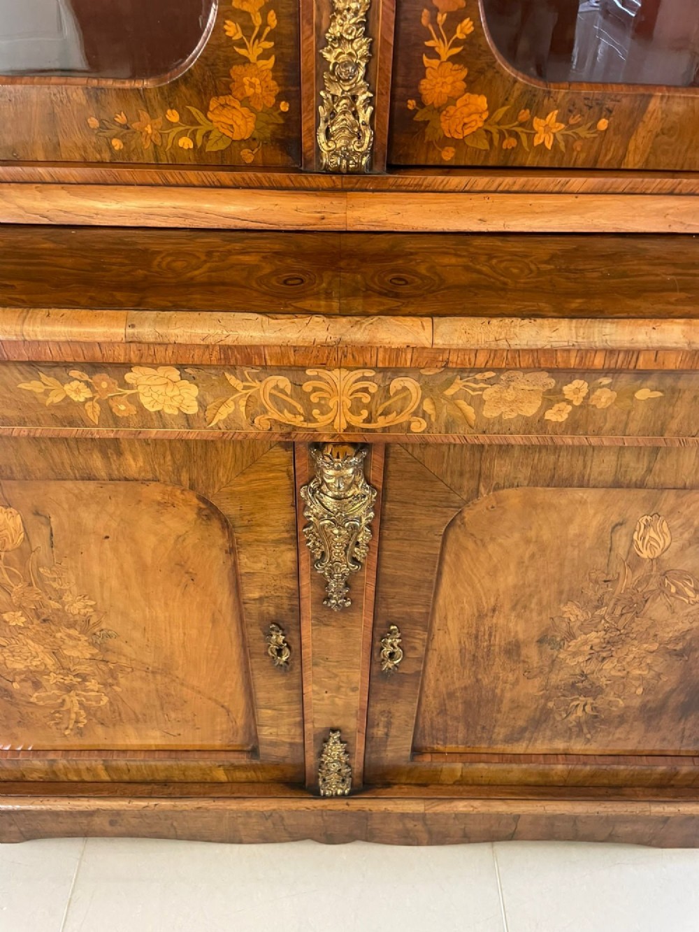 A Victorian two-part burr walnut bookcase cabinet featuring glazed upper doors with floral marquetry inlays and gilt ormolu mounts. View XI