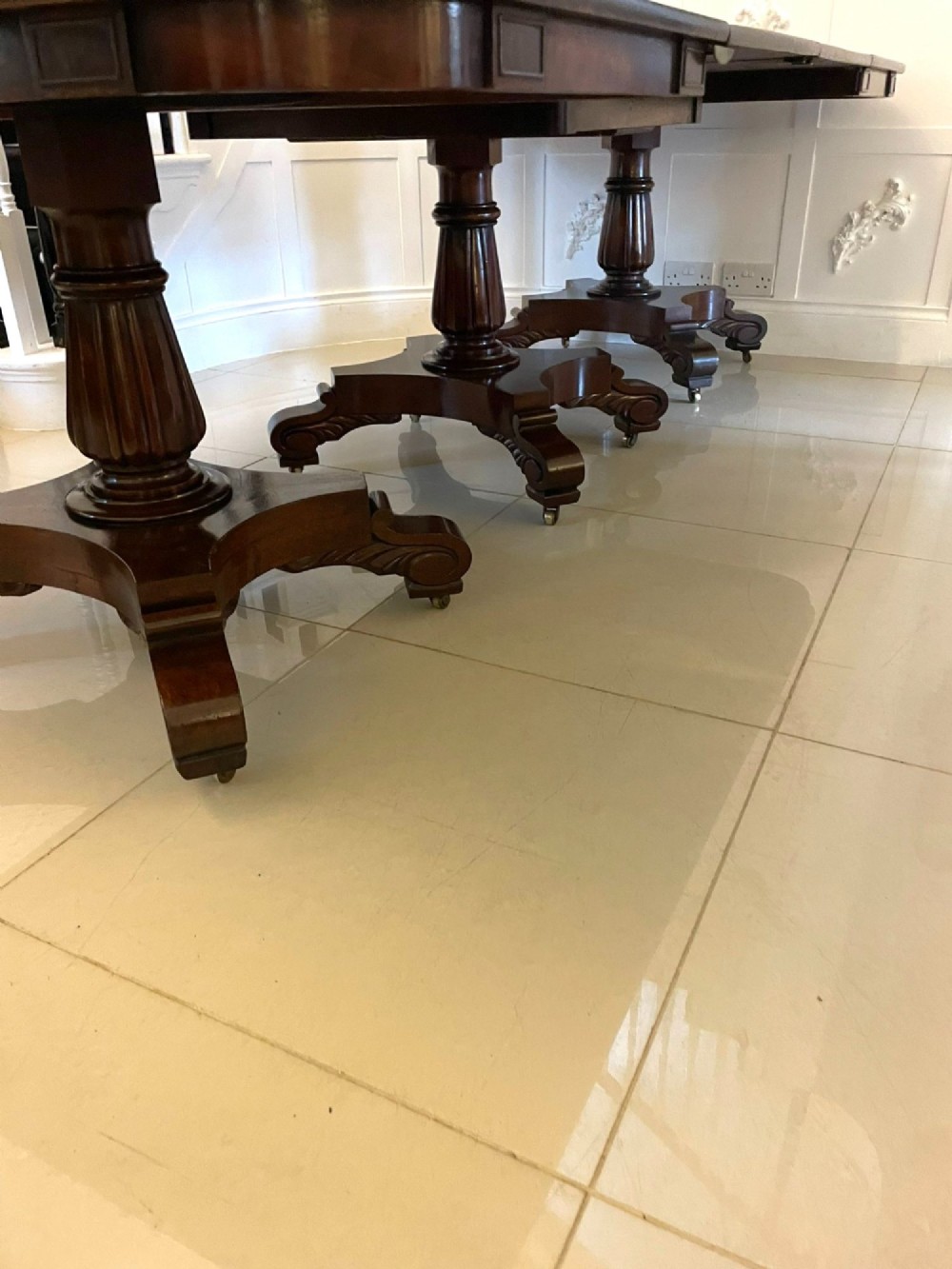 A large polished Regency style mahogany extendable dining table featuring a rounded rectangular top supported by carved pedestal bases on splayed legs. View V