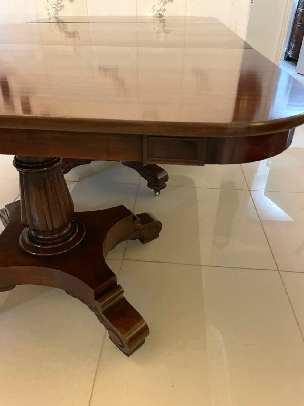A large polished Regency style mahogany extendable dining table featuring a rounded rectangular top supported by carved pedestal bases on splayed legs. View VI