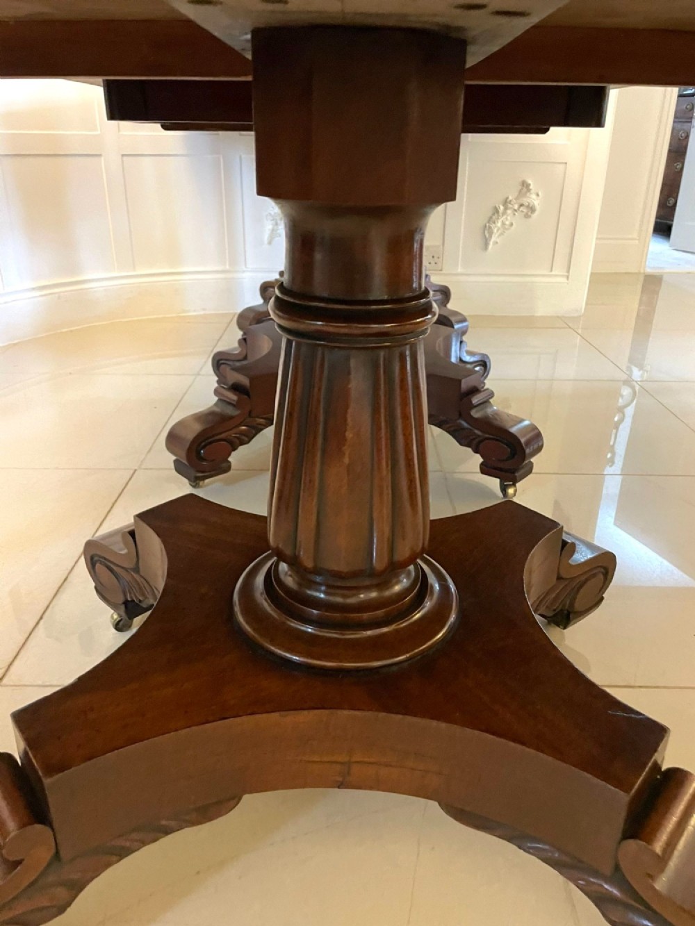 A large polished Regency style mahogany extendable dining table featuring a rounded rectangular top supported by carved pedestal bases on splayed legs. View VII