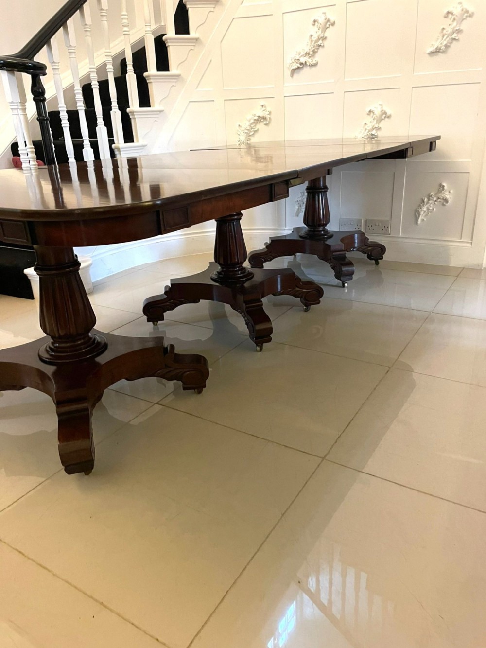 A large polished Regency style mahogany extendable dining table featuring a rounded rectangular top supported by carved pedestal bases on splayed legs. View IX