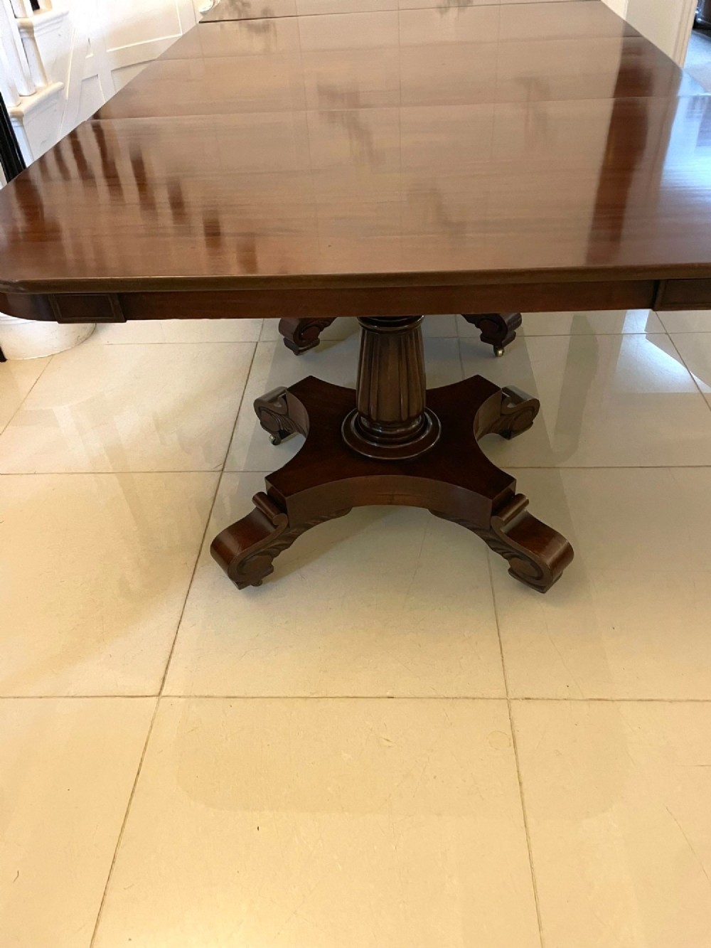 A large polished Regency style mahogany extendable dining table featuring a rounded rectangular top supported by carved pedestal bases on splayed legs. View XII