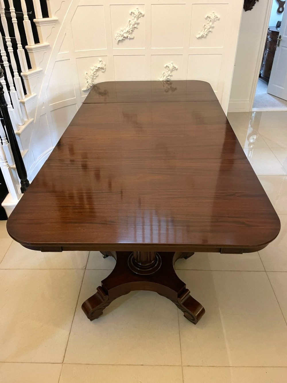 A large polished Regency style mahogany extendable dining table featuring a rounded rectangular top supported by carved pedestal bases on splayed legs. View XIII