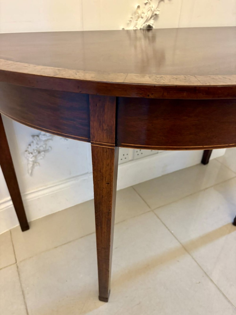 A pair of George III semi-circular mahogany console tables featuring crossbanded tops and square tapered legs. View IV