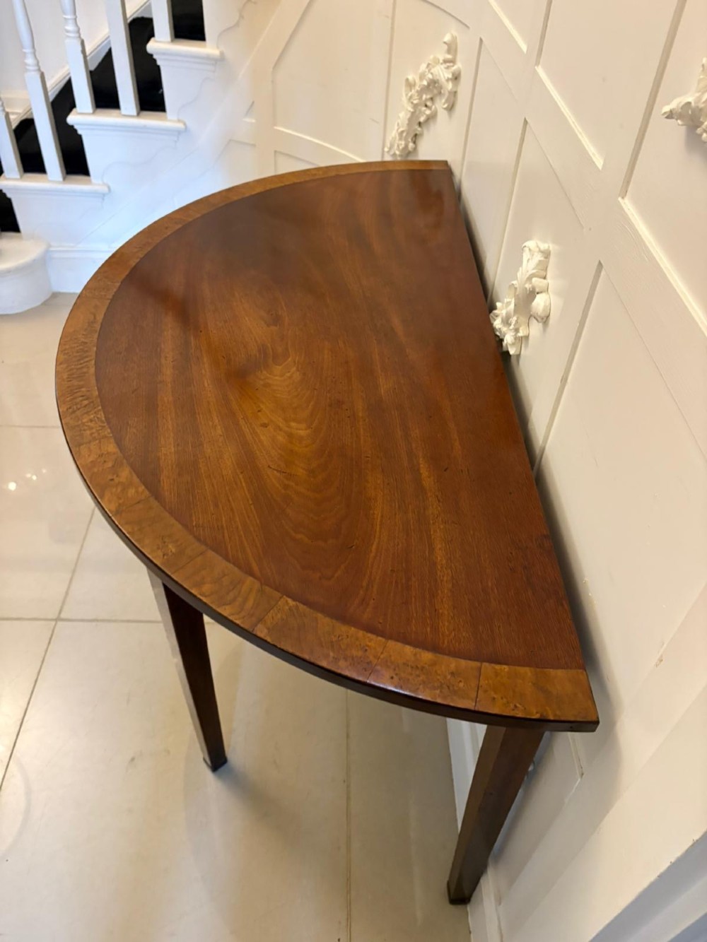 A pair of George III semi-circular mahogany console tables featuring crossbanded tops and square tapered legs. View VI