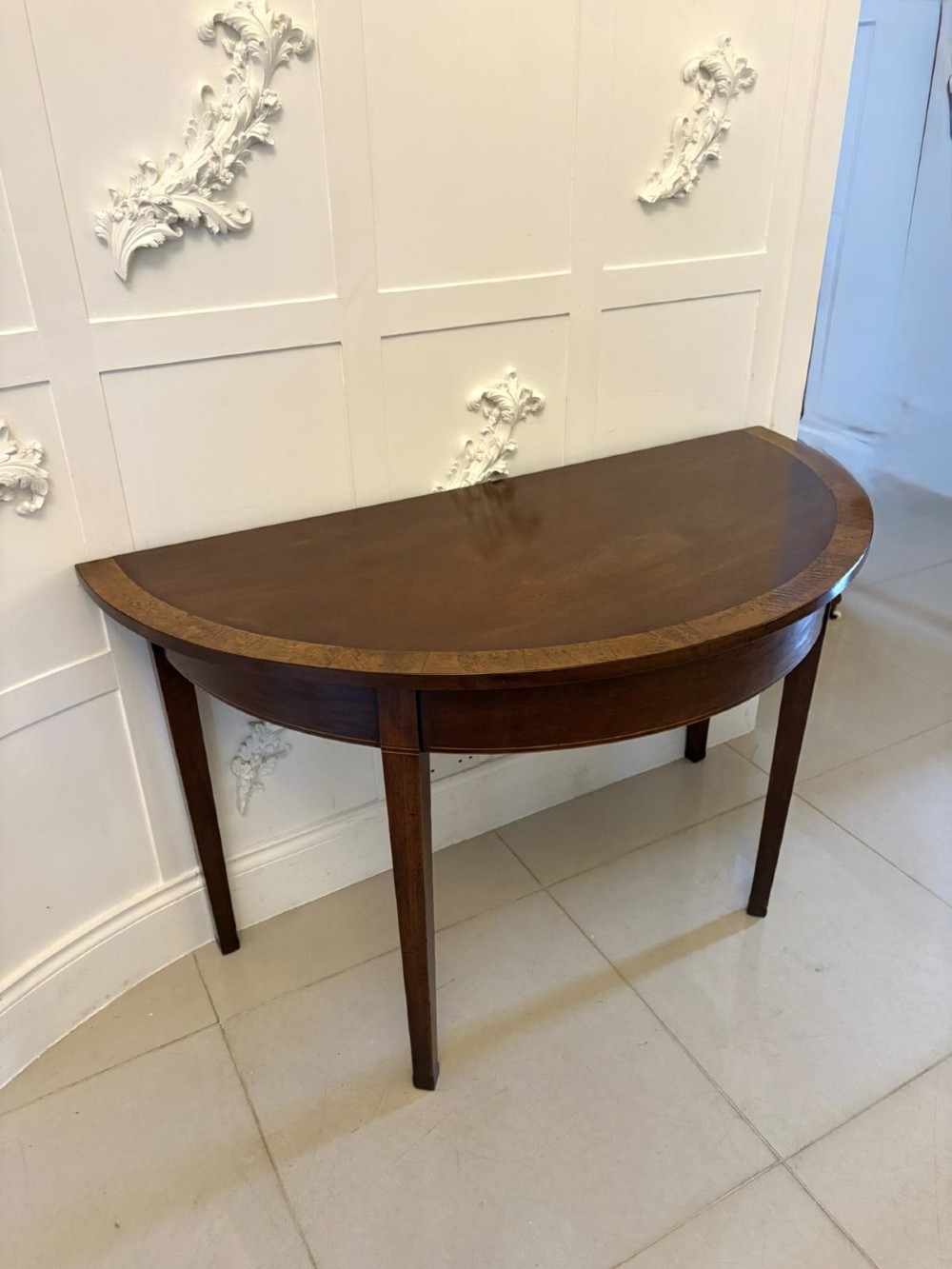 A pair of George III semi-circular mahogany console tables featuring crossbanded tops and square tapered legs. View IX