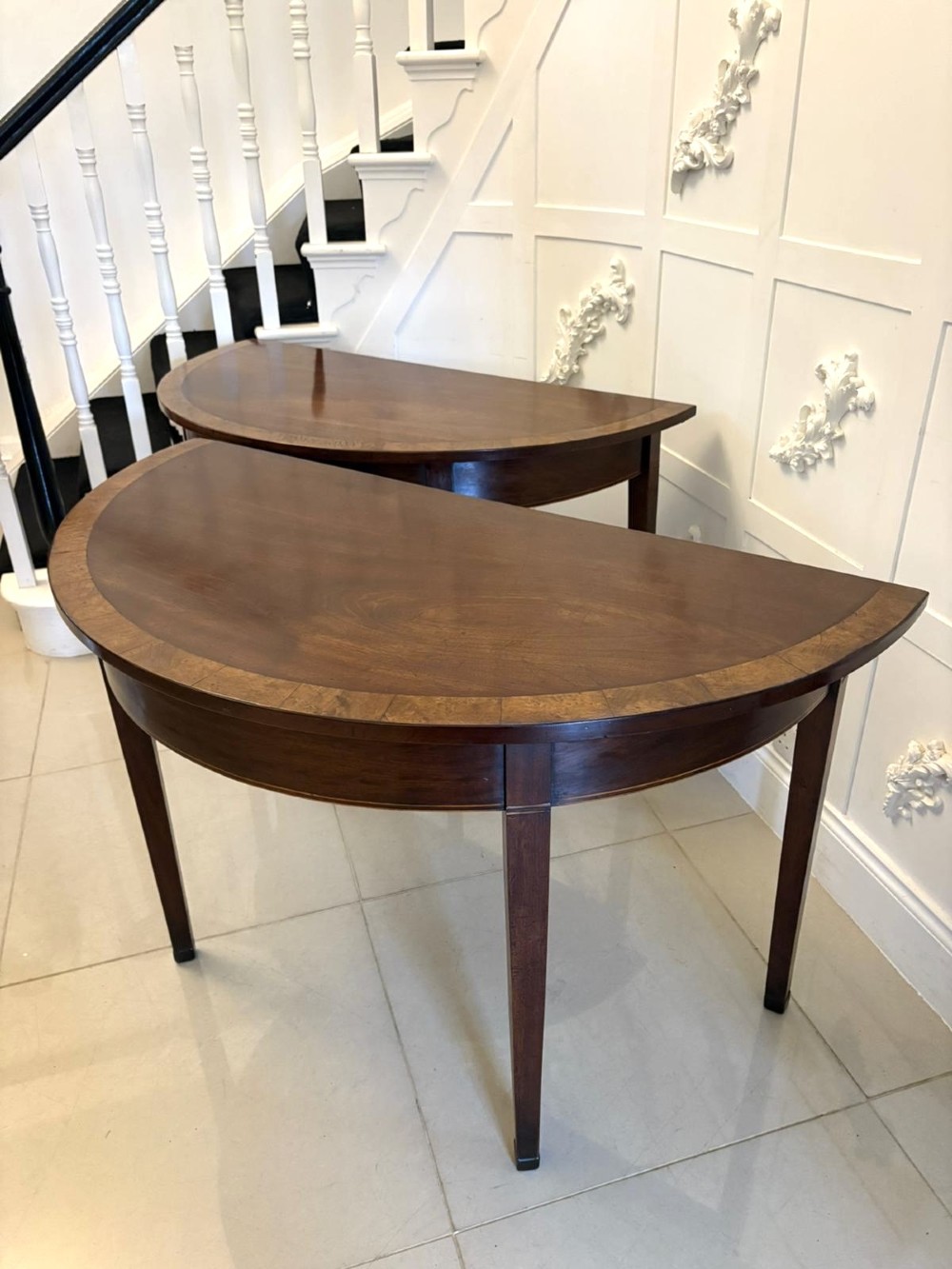 A pair of George III semi-circular mahogany console tables featuring crossbanded tops and square tapered legs. View XI